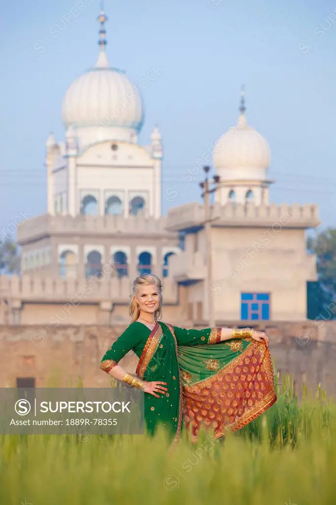 Portrait of a blond woman wearing a sari in a field with a temple in the background, ludhiana punjab india