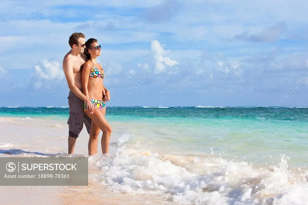 A couple wearing swimsuits stand in the ocean holding hands, punta cana la altagracia dominican republic
