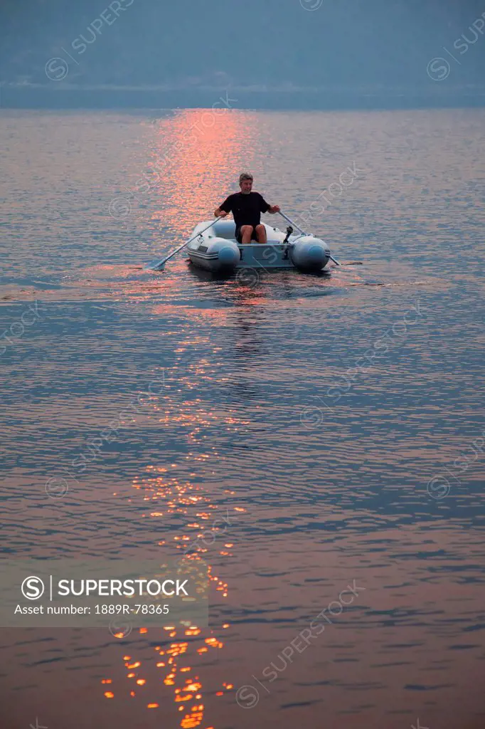 A man rows his dinghy in pendrell sound as the sun sets, british columbia canada