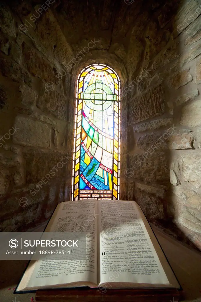 An open bible and a stained glass window in st. mary´s church, holystone northumberland england