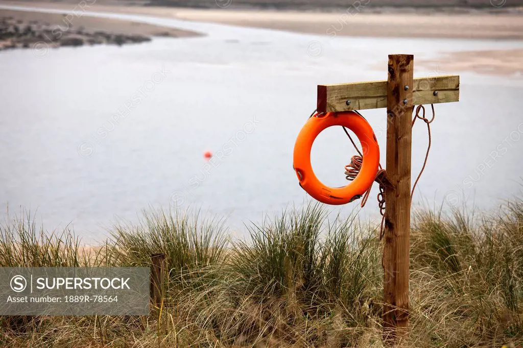 An orange life preserver hangs on a wooden structure at the water´s edge, alnmouth northumberland england