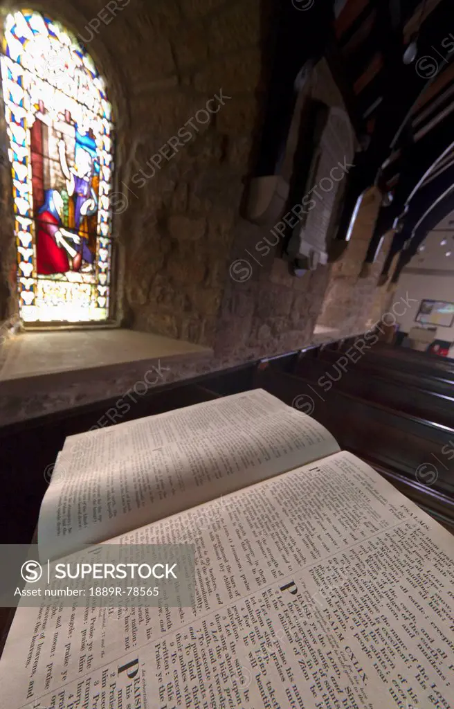 An open bible on a podium and a stained glass window in st. mary´s church, holystone northumberland england
