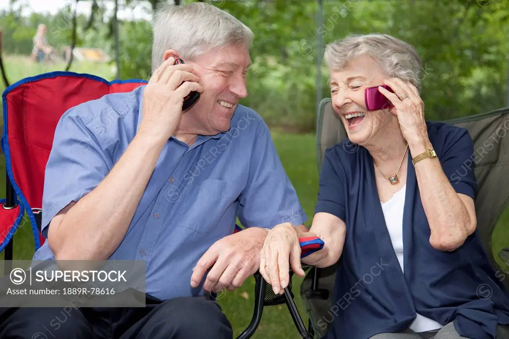 a senior man and woman sitting side by side and each talking on a cell phone, edmonton, alberta, canada