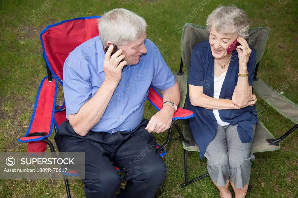 a senior man and woman sitting side by side and each talking on a cell phone, edmonton, alberta, canada
