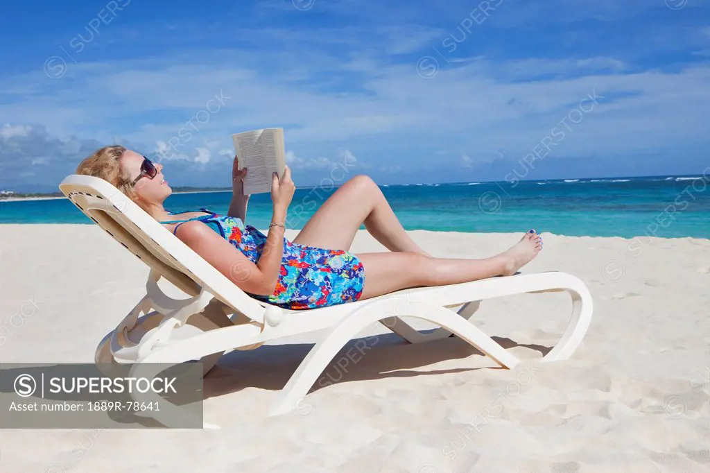 A woman reads a book on a beach chair by the ocean, punta cana la altagracia dominican republic