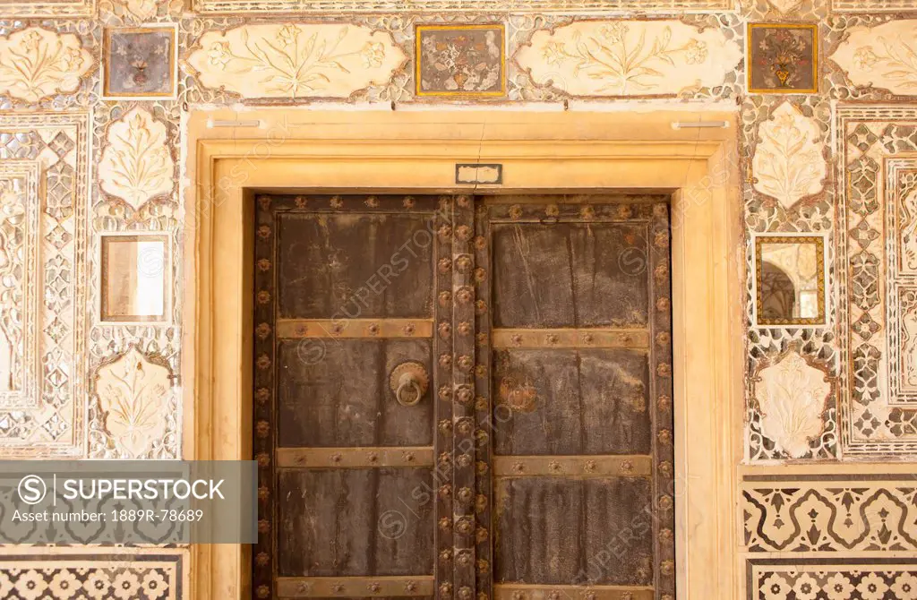 Wooden door with rivets and walls with ornate tile at amer fort, jaipur rajasthan india