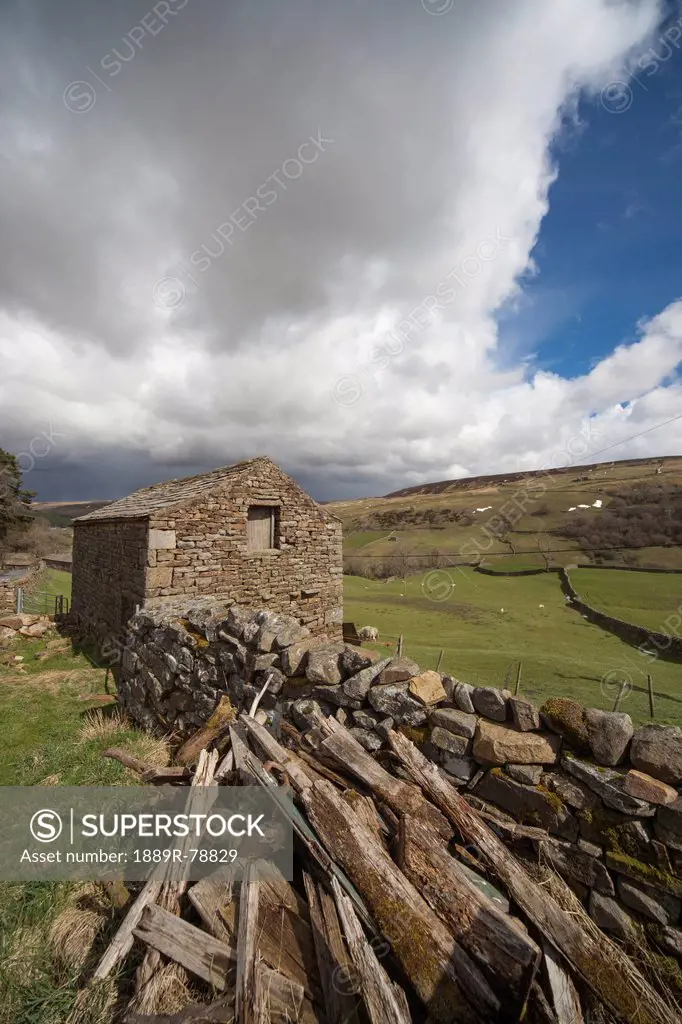 A pile of wood laying beside a stone wall and a stone building, swaledale england