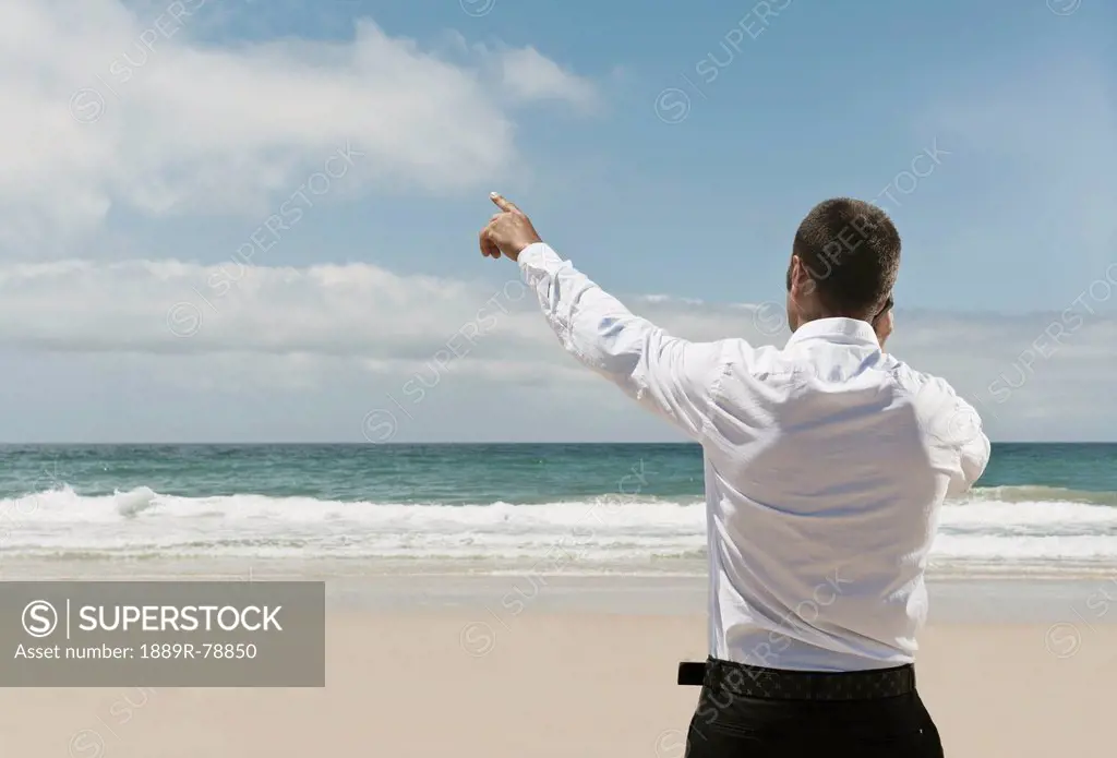 A Businessman On The Beach Talking On His Cell Phone And Pointing To The Sky, Tarifa Cadiz Andalusia Spain