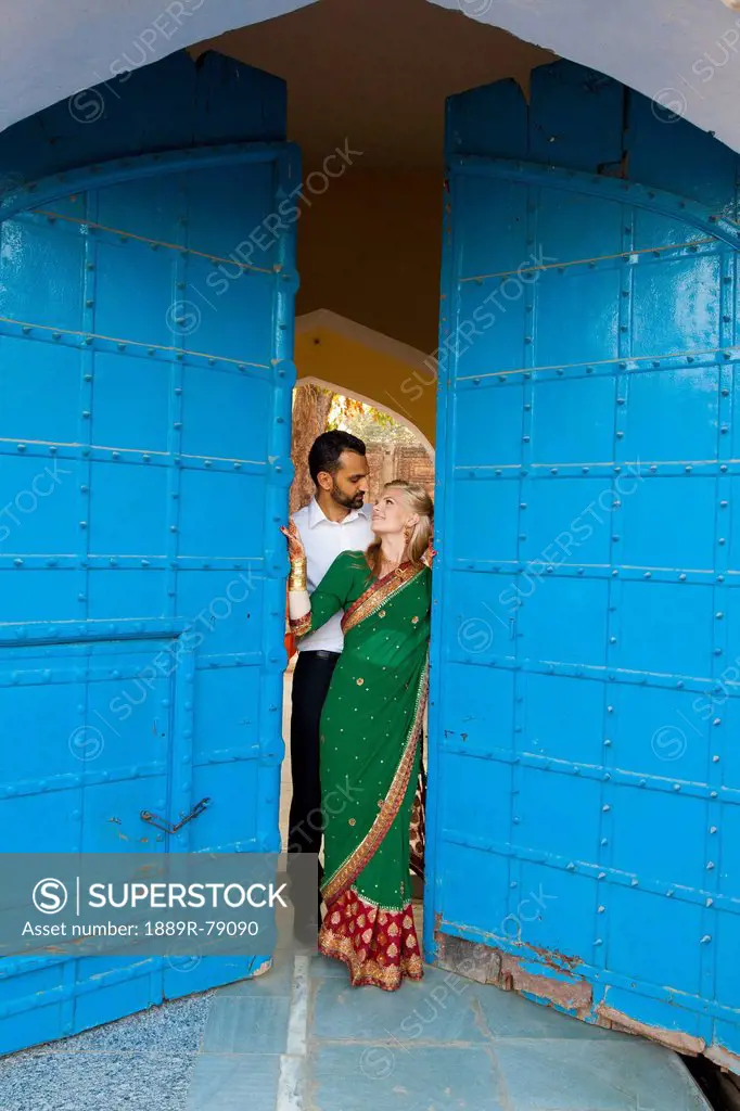 Portrait of a mixed race couple with her wearing a sari standing in the doorway with large blue doors, ludhiana punjab india
