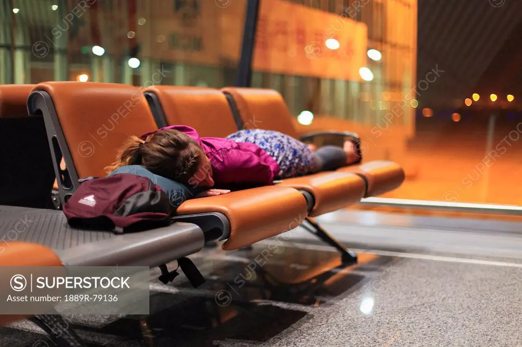 a girl sleeping on chairs at an airport, beijing, china