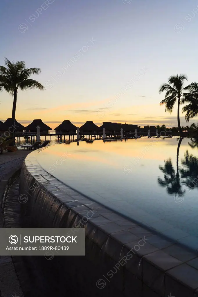 Sunset and palm trees reflecting in a pool at the bora bora nui resort and spa, bora bora island society islands french polynesia south pacific