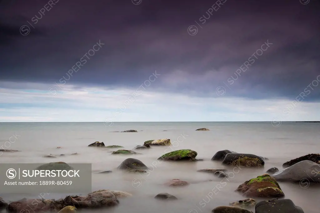 Rocks in tranquil water under storm clouds, northumberland england