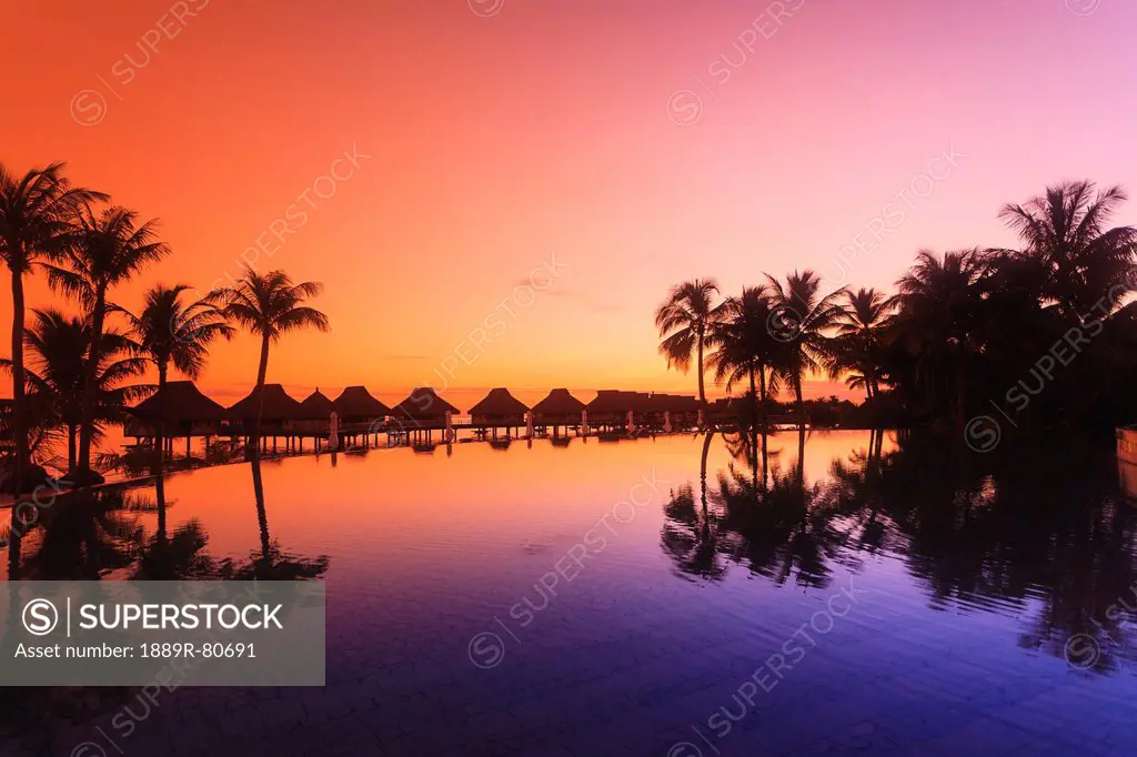 Sunset and palm trees reflecting in a pool at the bora bora nui resort and spa, bora bora island society islands french polynesia south pacific