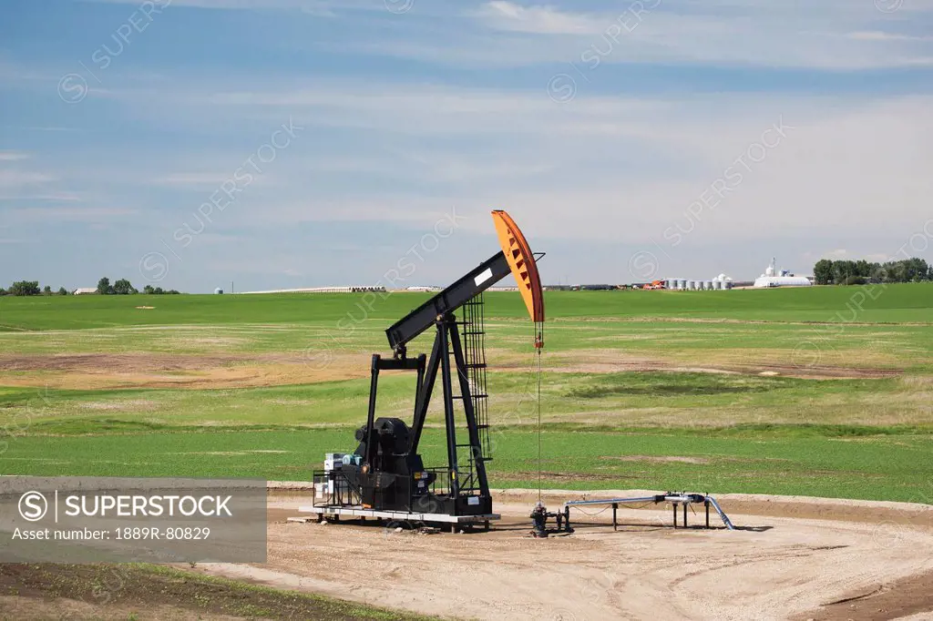Pumpjack in a field with clouds and blue sky east of airdrie, alberta canada