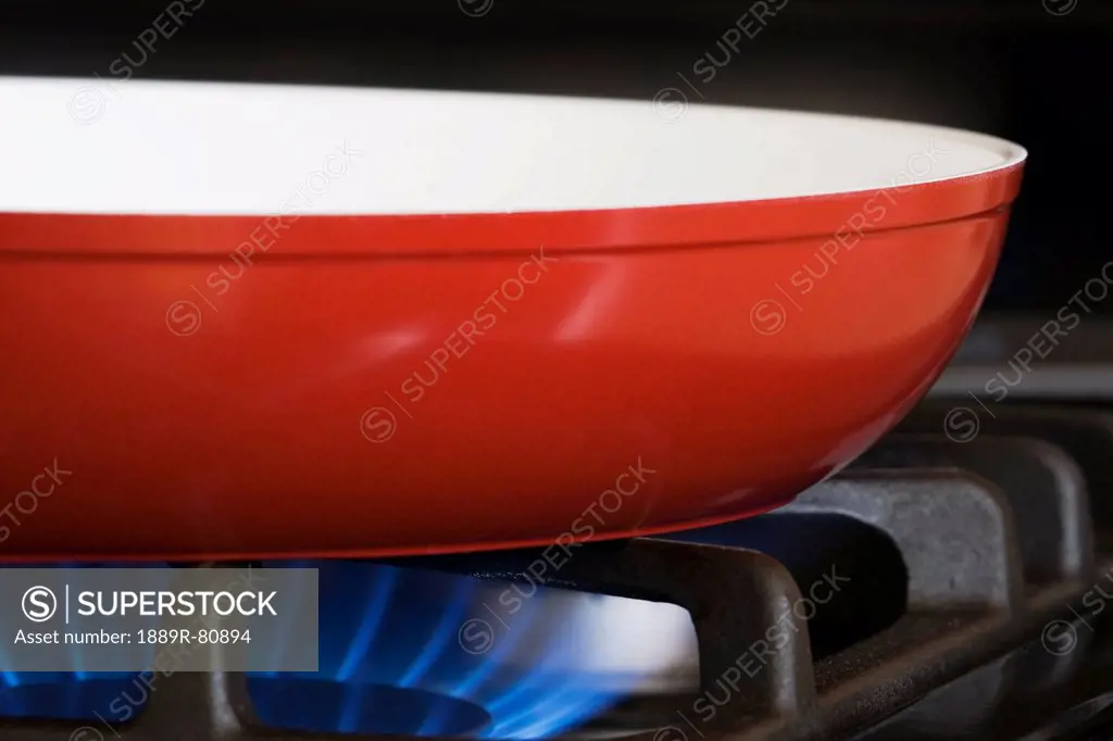 Close up of a red frying pan on a gas stove with blue gas burner, calgary alberta canada