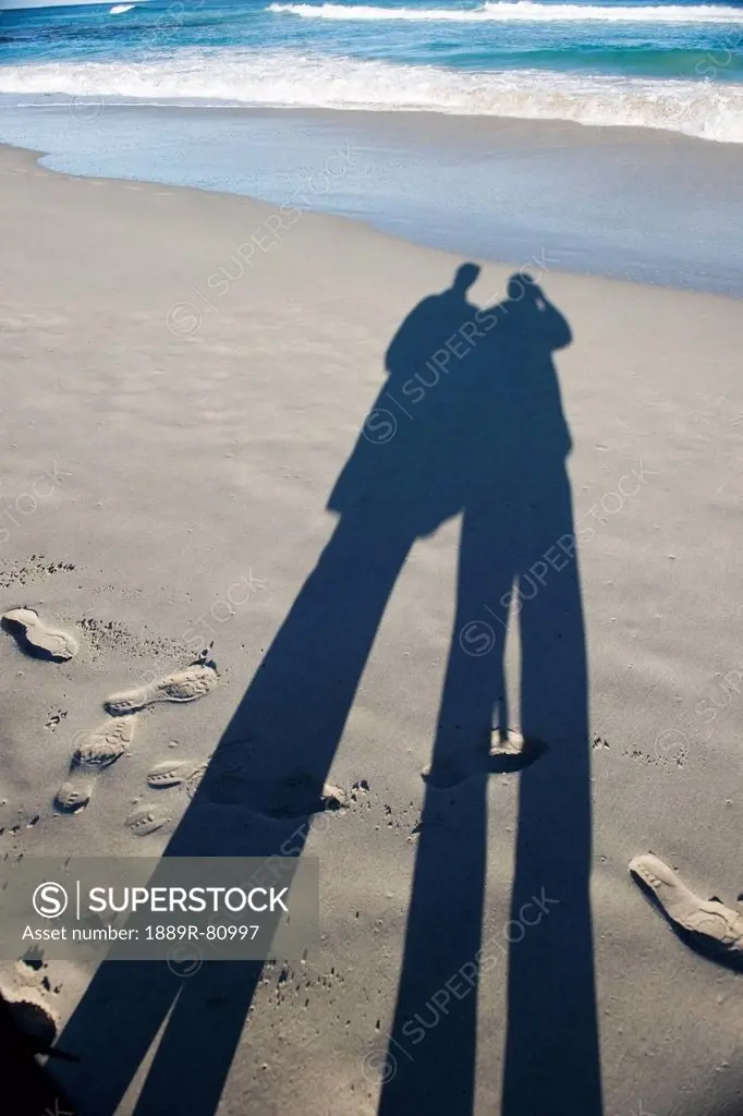 Long shadows of two people standing on a beach at the water´s edge, australia