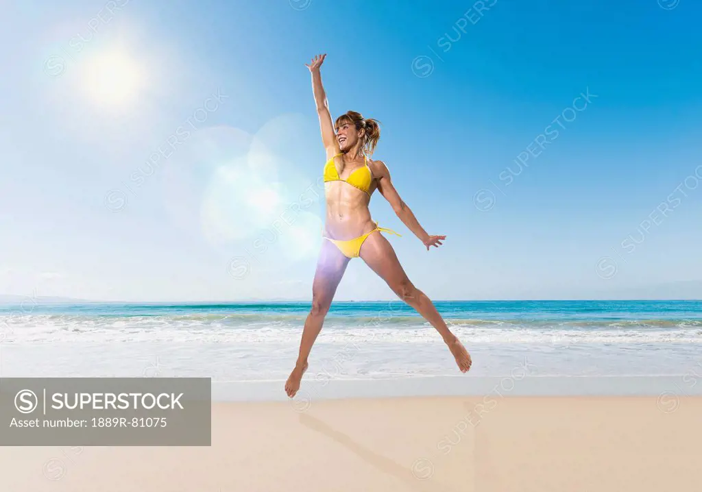 A woman in a yellow bikini jumps in the air on the beach, tarifa cadiz andalusia spain