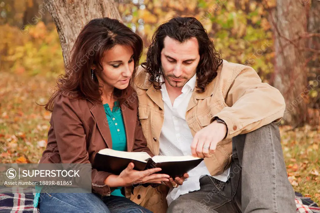 Married couple reading bible together in a park in autumn, edmonton, alberta, canada