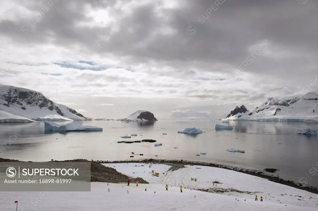 People standing on the ice with icebergs and mountains along the coastline, antarctica
