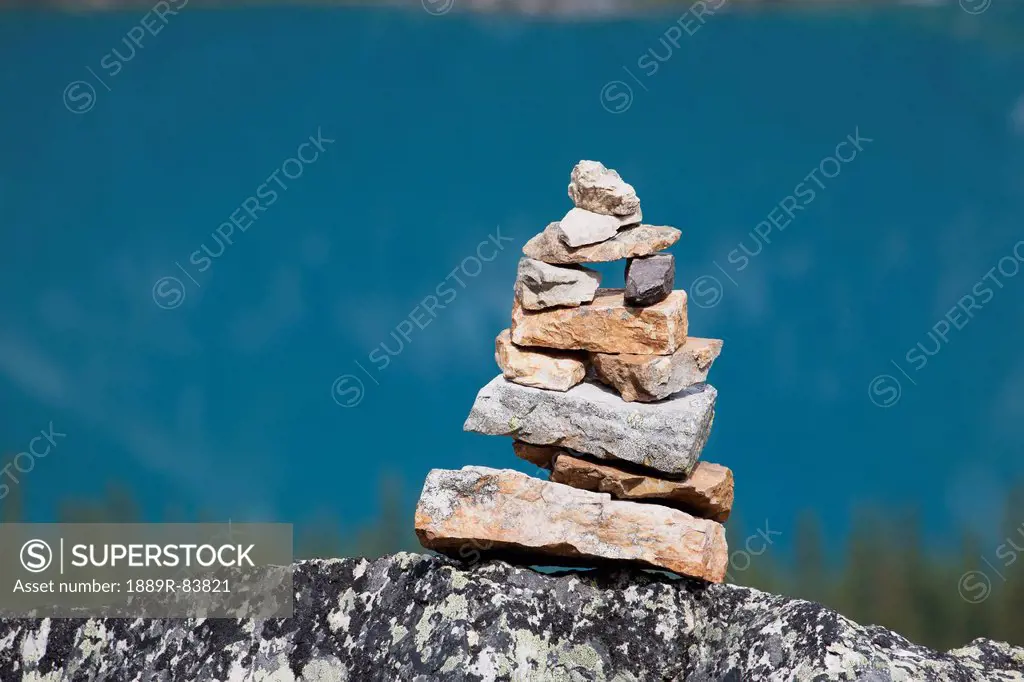 Close Up Of Rock Cairn Sitting On A Rock With Blue Lake In Background, Field British Columbia Canada