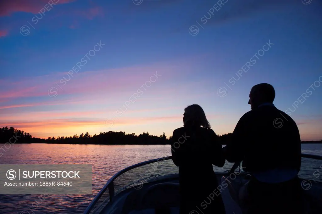Middle aged couple travelling by motorboat in the lake of the woods at sunset, kenora ontario canada
