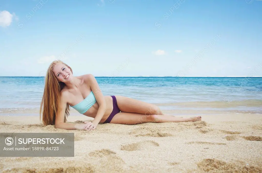 A young woman laying on the sand at the ocean´s edge, kauai hawaii united states of america