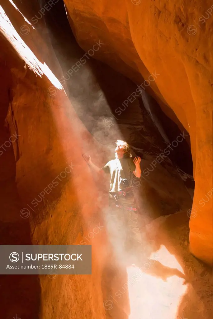 Man looking up into a sunbeam streaming into a slot_canyon, san rafael swell utah united states of america