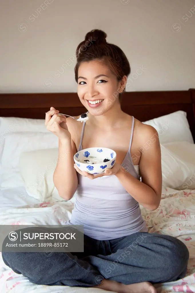 A girl sitting on her bed eating a snack from a bowl, berkeley california united states of america
