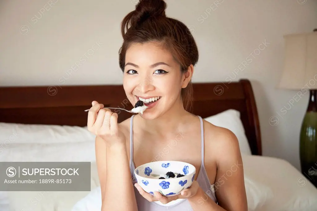 A girl sitting on her bed eating a snack from a bowl, berkeley california united states of america