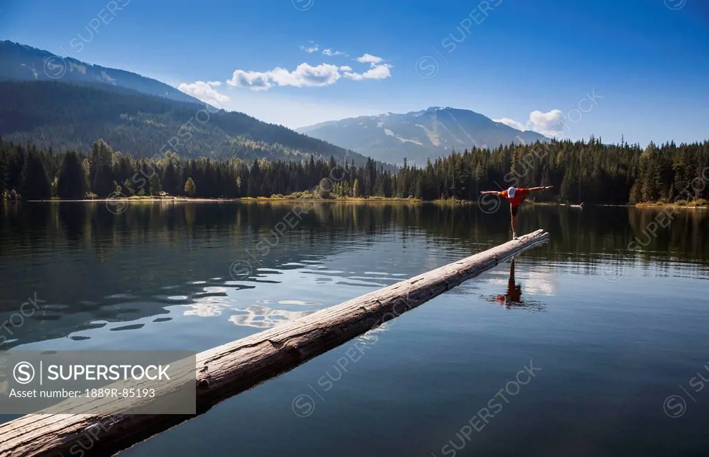 A man practises yoga on a log boom in lost lake, whistler british columbia canada