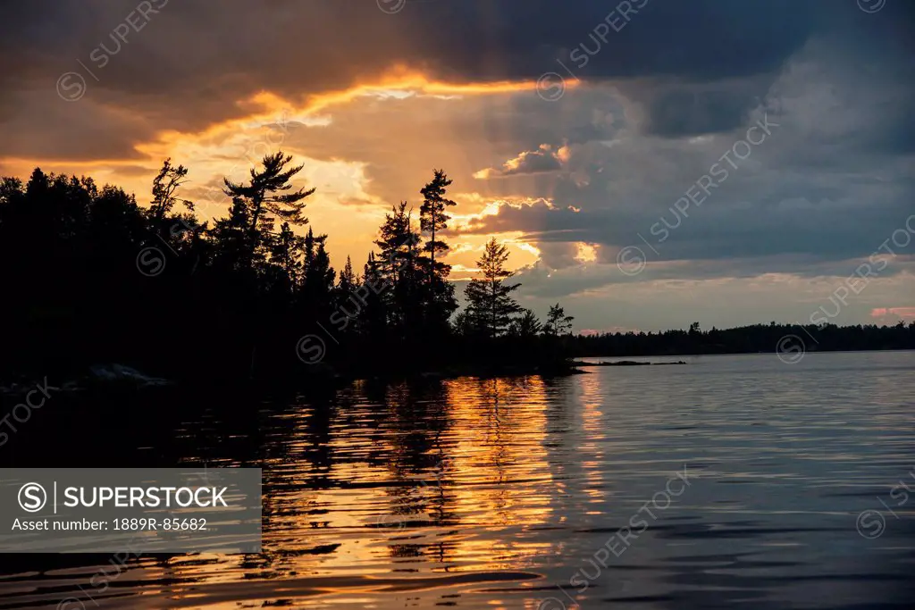 Reflection Of The Sun Setting Over A Lake And Storm Clouds, Keewatin Ontario Canada