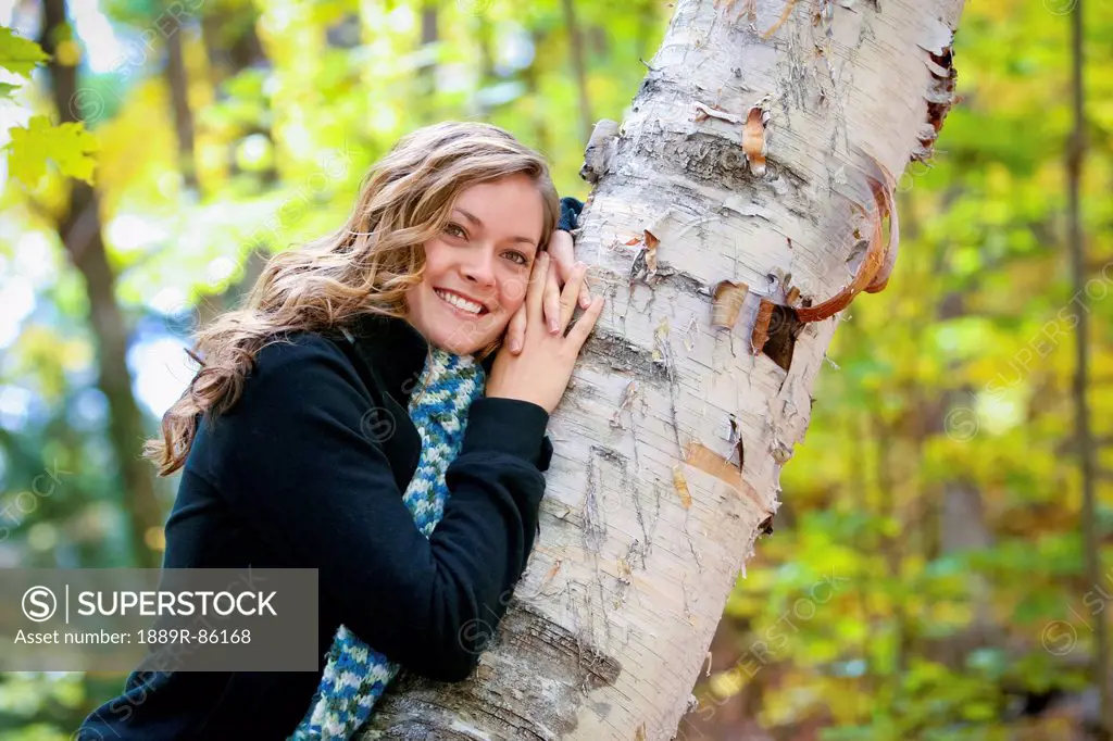 Portrait Of A Young Woman Leaning Against A Tree Trunk In A Forest, Ontario Canada