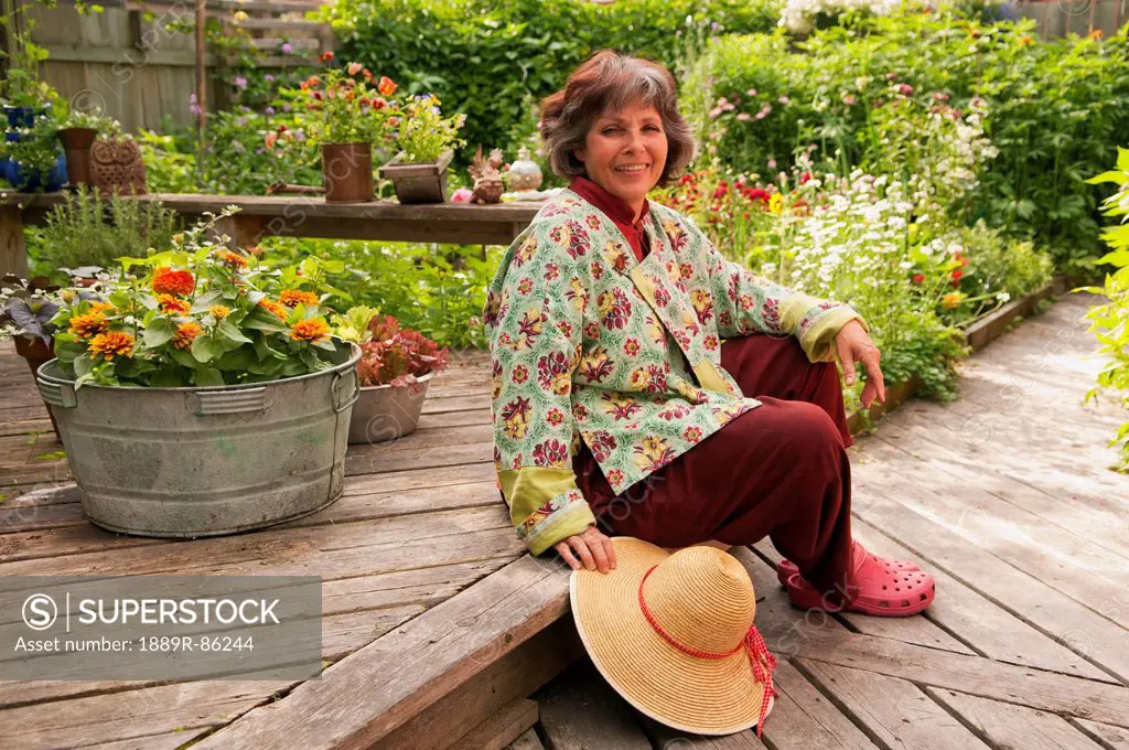 A Woman Sitting On Her Backyard Deck Surrounded By Plants And Flowers, Winnipeg Manitoba Canada
