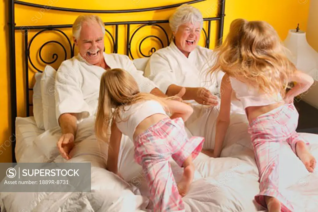 Grandparents playing with their granddaughters in a bed.