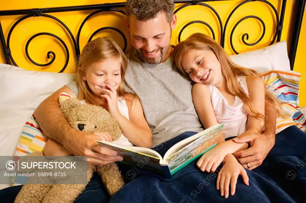 A father reading to his children in bed.