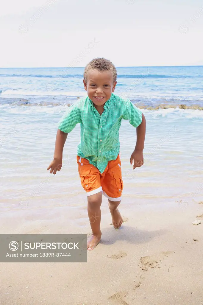 A Young Boy Running In The Sand By The Ocean;Hawaii United States Of America