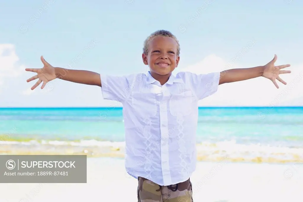 A Young Boy Poses With Arms Outstretched On The Beach At The Water's Edge;Hawaii United States Of America