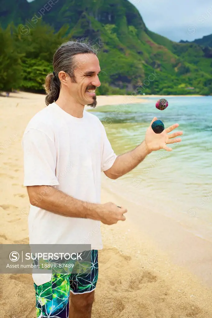A Man Juggles With Hackey Sacks While Standing On The Beach At The Water's Edge;Hawaii United States Of America