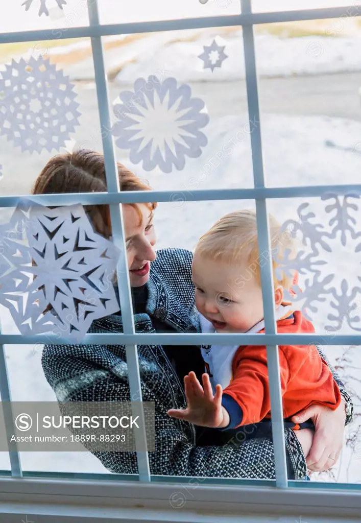 A mother and young son standing at the front window of their house with snowflakes on it;Willimantic connecticut united states of america