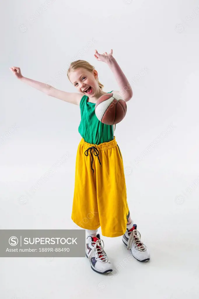 A young girl wearing oversized basketball jersey shorts and shoes throwing a basketball;Anchorage alaska united states of america