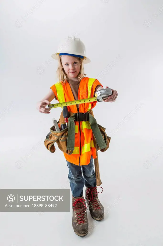 Young girl wearing oversized construction clothes and hard hat holding a tape measure;Anchorage alaska united states of america