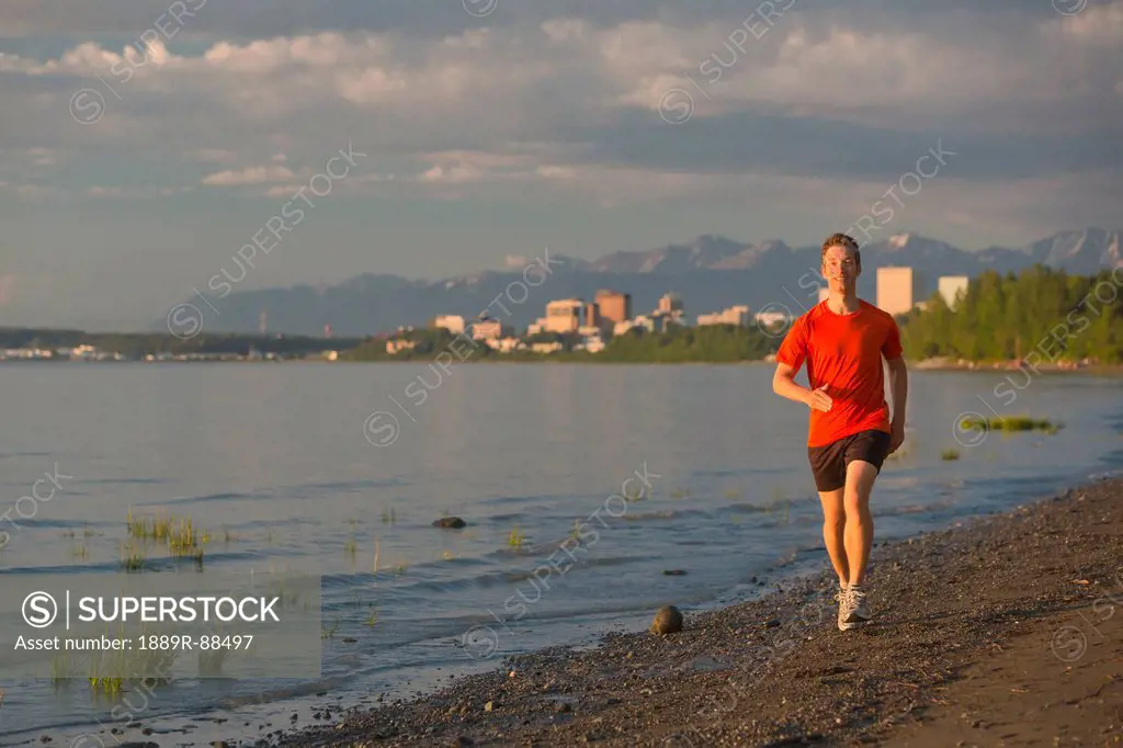 Man jogging on the beach next to the tony knowles coastal trail during high tide at sunset;Anchorage alaska united states of america