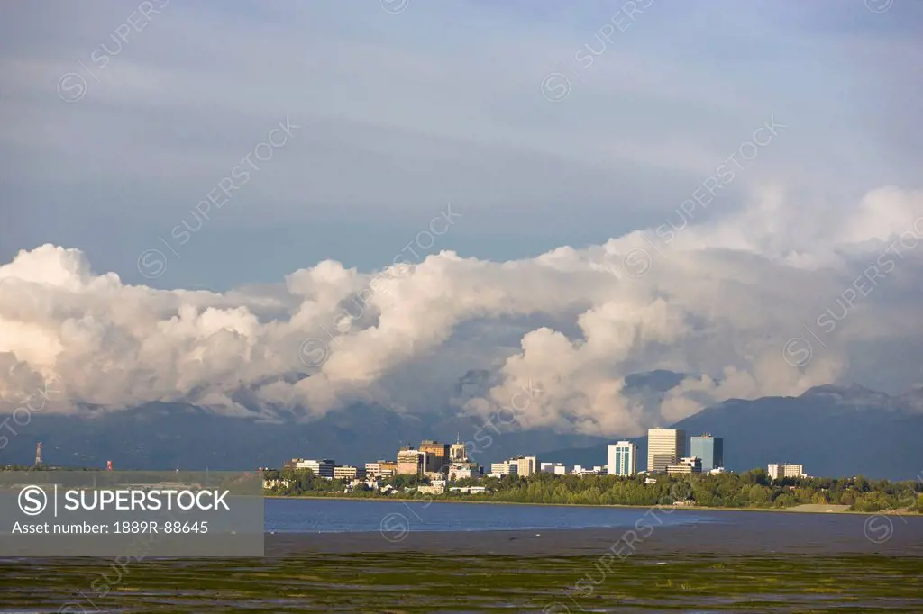Late Afternoon Light Shines Through Clouds Onto The Downtown Anchorage Skyline After A Thunderstorm, Southcentral Alaska, Summer