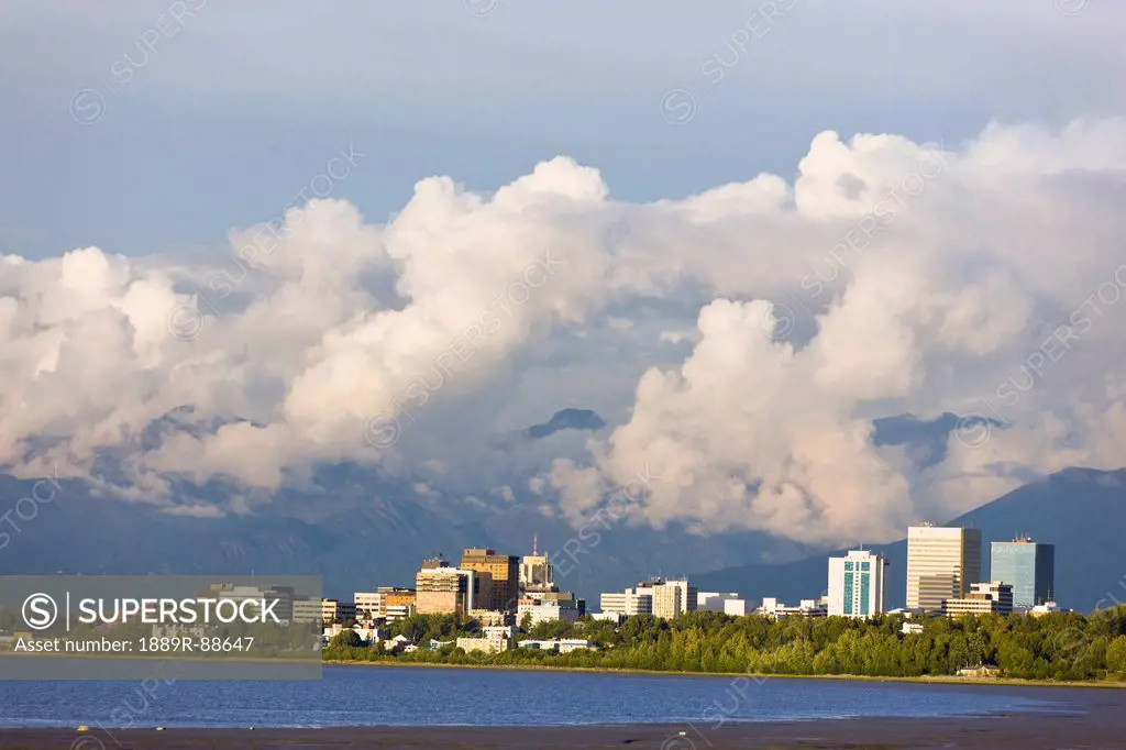 Late Afternoon Light Shines Through Clouds Onto The Downtown Anchorage Skyline After A Thunderstorm, Southcentral Alaska, Summer