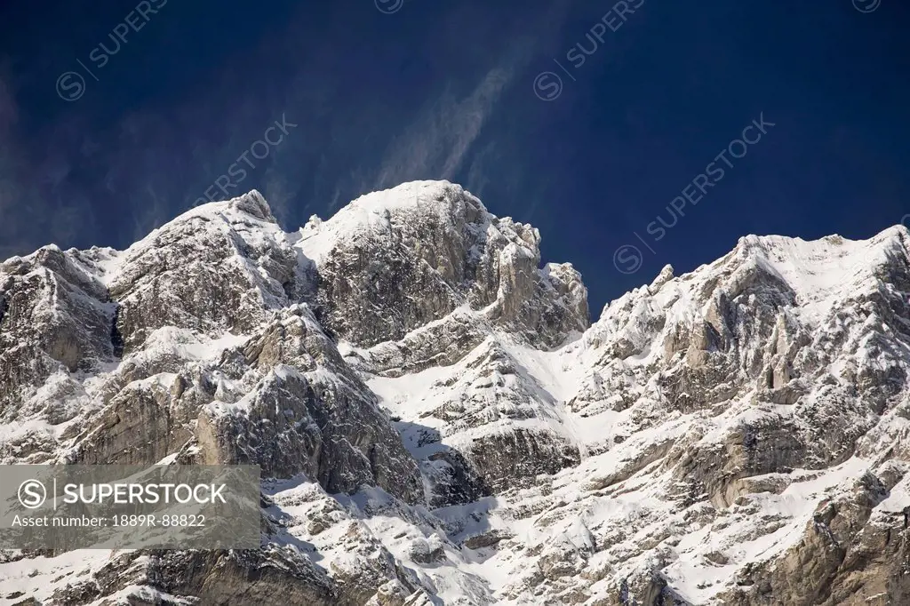 Snow covered mountain peak with snow blowing off peak and blue sky;Banff alberta canada