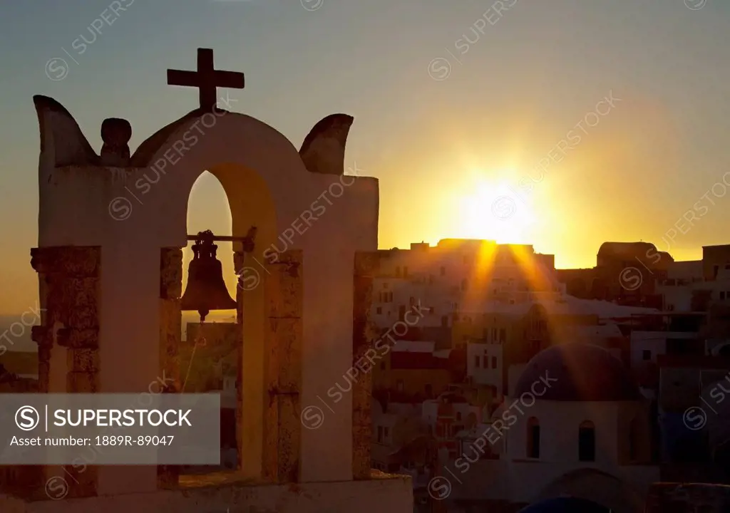 Cross and bell on a structure at sunset;Oia greece