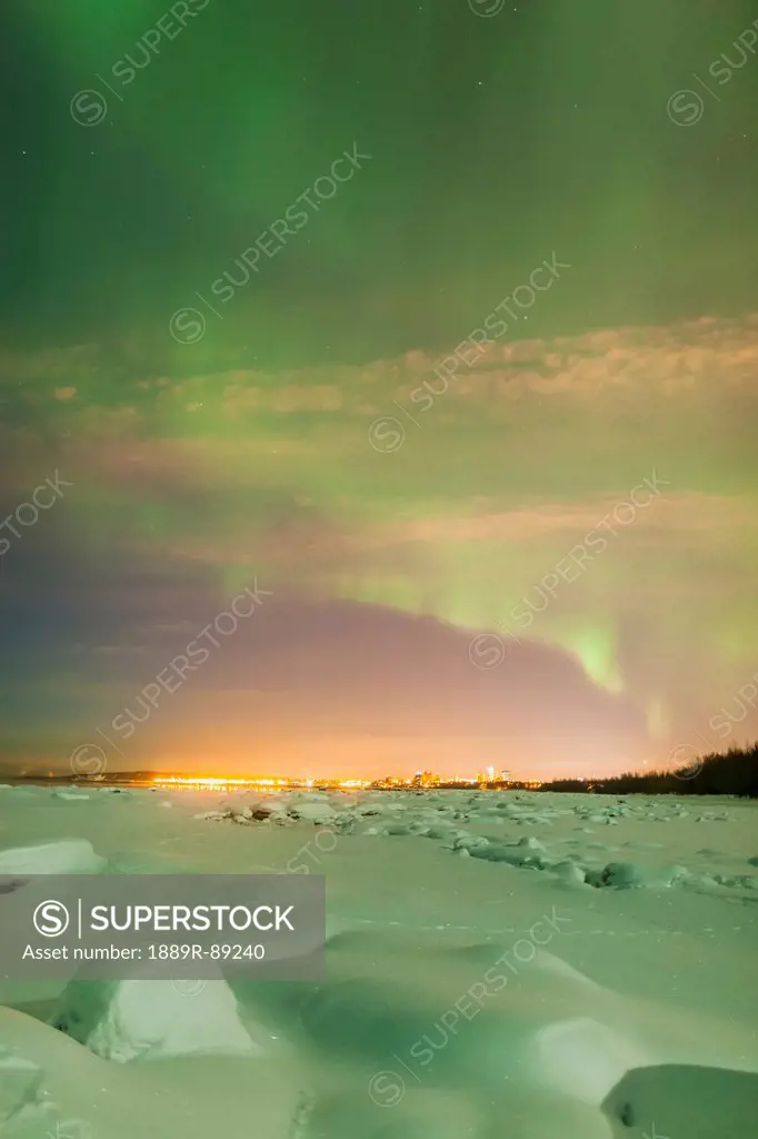 The northern lights shine above the anchorage city skyline and light the snow green in this nighttime view from the tony knowles coastal trail in wint...
