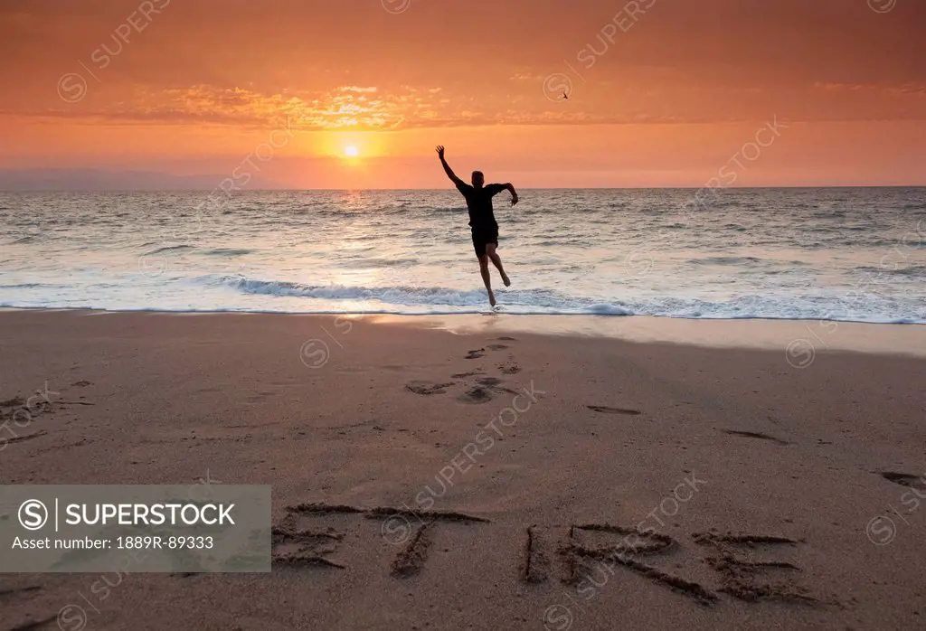 A man leaps for joy on a tropical beach with the word retire written in the sand;Puerto vallarta mexico