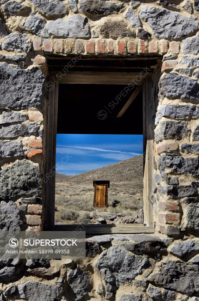 Gold mining ghost town outhouse in distance framed through stone building window;Bodie california united states of america