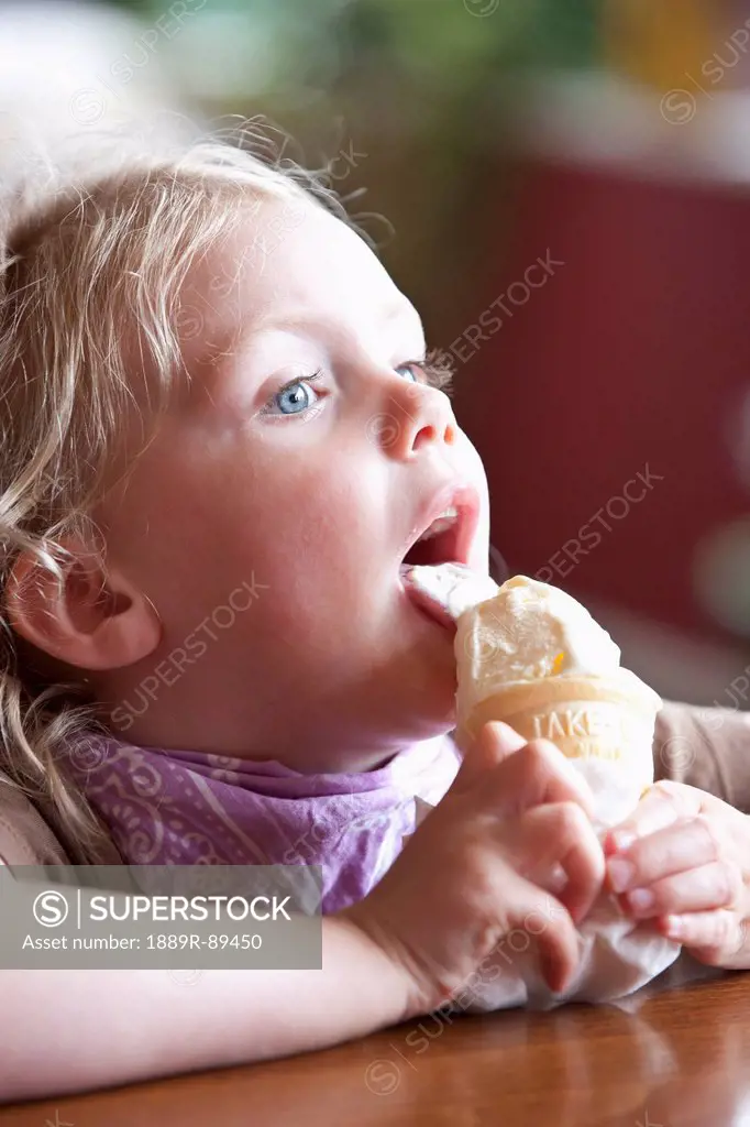 Young girl eating a ice cream cone while sitting in a coffe shop on a rainy day in Seward, summer, Seward, Southcentral Alaska, USA